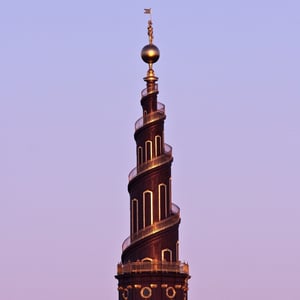 Spiraltårnet på Vor Frelsers Kirke i København ved solnedgang med en gylden statue på toppen.