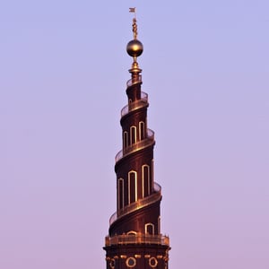 Spiraltårnet på Vor Frelsers Kirke i København ved solnedgang med en gylden statue på toppen.